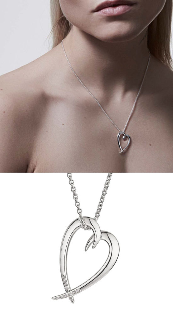 A sterling silver heart-shaped pendant on a chain. The heart is formed by two hook shapes. The heart is open in the middle. The chain goes through the opening. The lower part of the heart is finished with diamonds.